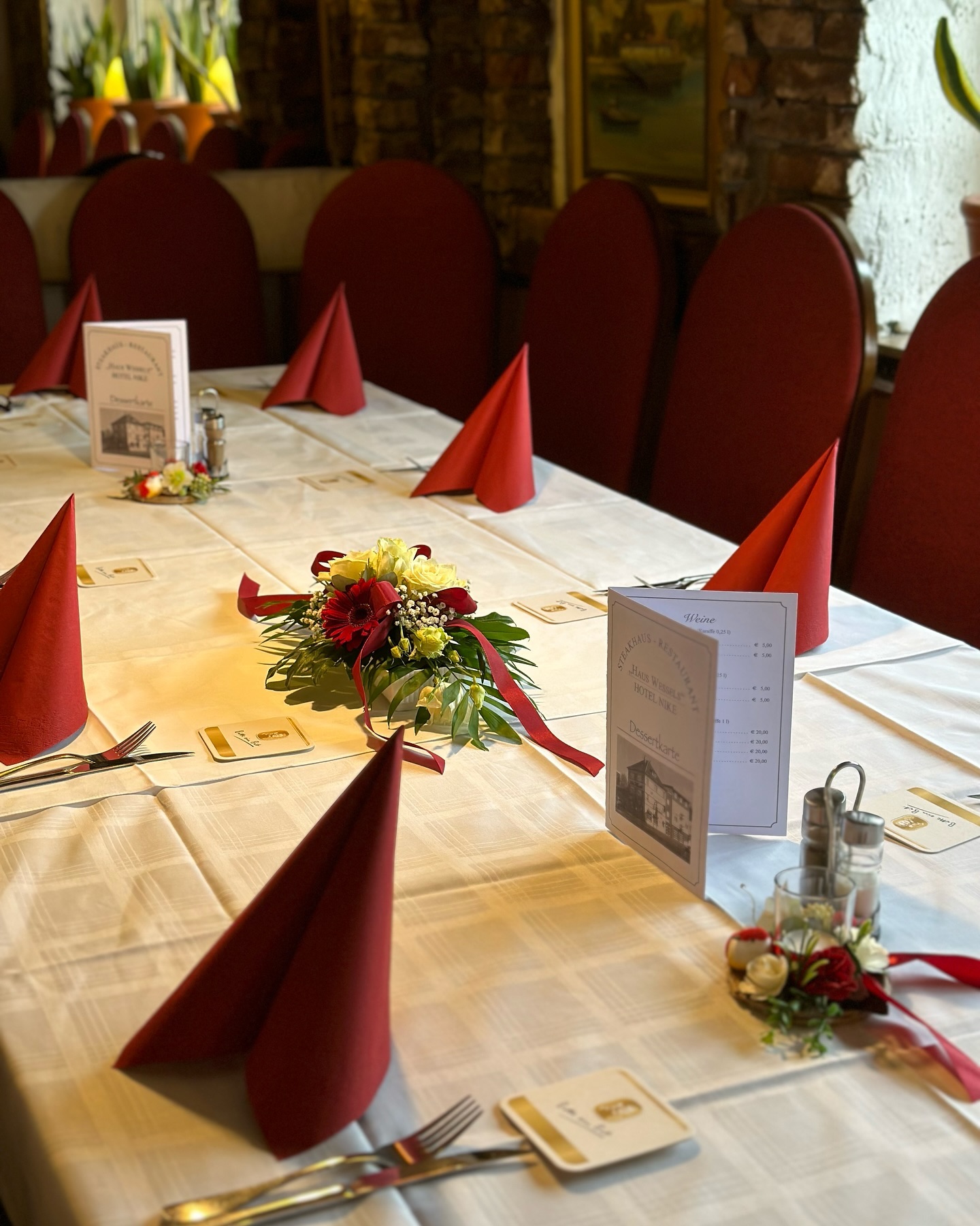 Gedeckte Tafel mit roten Servietten, Blumengesteck und Menükarte
