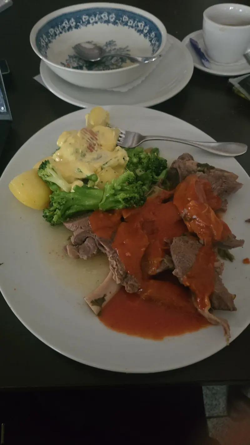 Tellergericht: Fleisch mit roter Sauce, Kartoffeln und Salat, dahinter eine Suppe