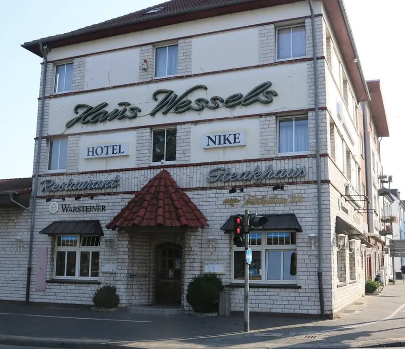 Haus Wessels bei Tag: weiß gekachelte Fassade mit den Schriftzügen Haus Wessels, Restaurant und Steakhaus, Eingang unter dem Ziegeldach