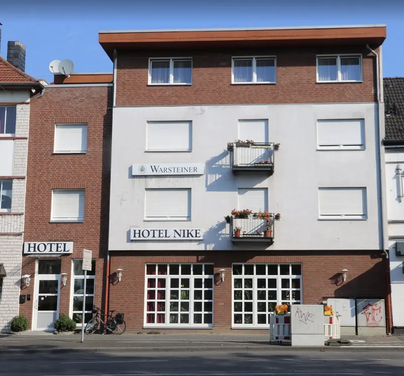 Hotel Nike von der Straße: weiße Fassade über rotem Backstein, Schild Hotel Nike, links der eigene Hoteleingang mit Schild Hotel