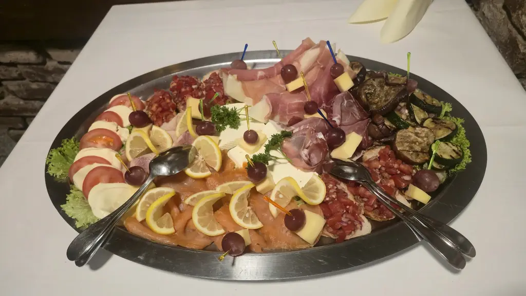 Große Platte mit Schinken, Salami, Käse, Lachs, Zitronen und gegrilltem Gemüse auf einem weiß gedeckten Tisch