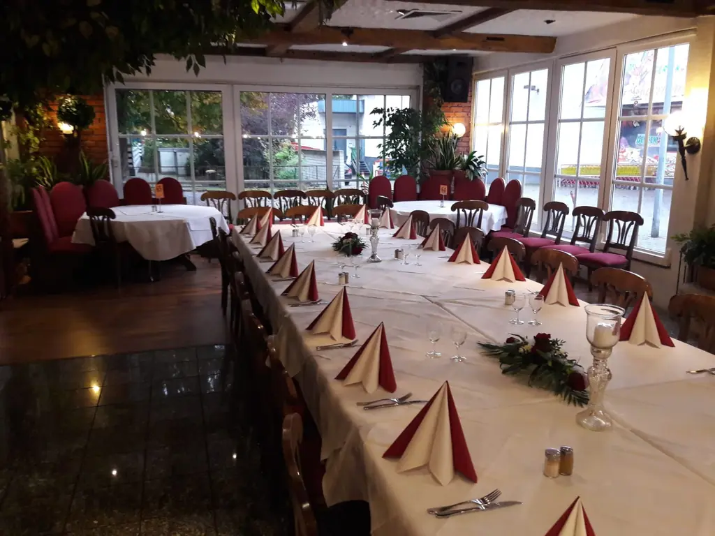 Lange, festlich gedeckte Tafel mit weißen Tischdecken und roten Servietten im Saal